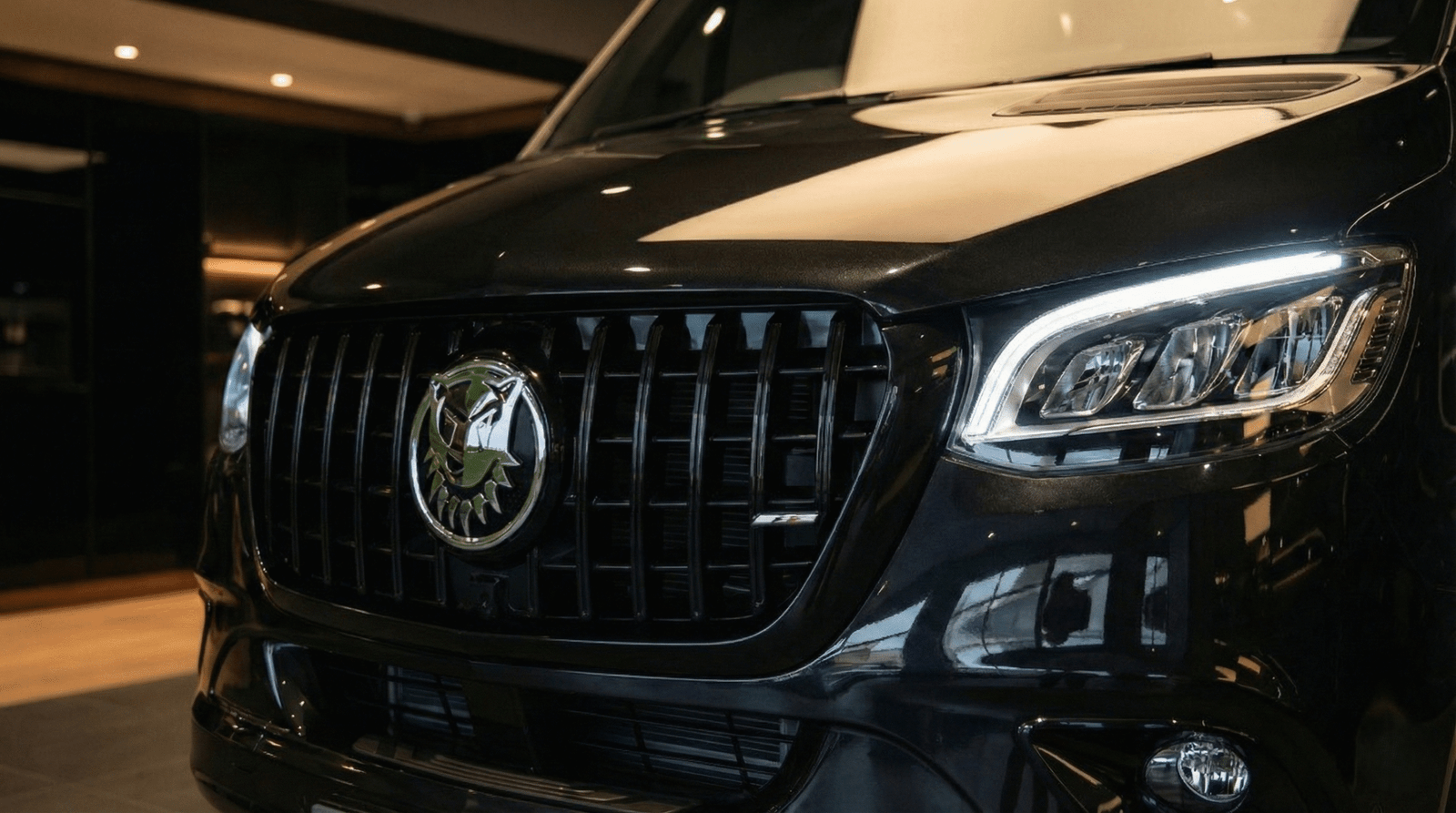 Czarny Mercedes-Benz Sprinter w wersji VIP widoczny z przodu. Luksusowy bus z czarnym grillem Panamericana i felgami premium. Wynajem busów dla delegacji i grup biznesowych w Panther Cars.